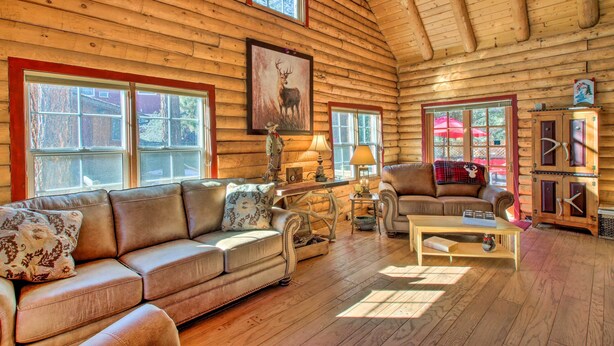 Ein Holzblockhaus-Interieur mit einem Ledersofa, einem Holztisch und einem Kamin.