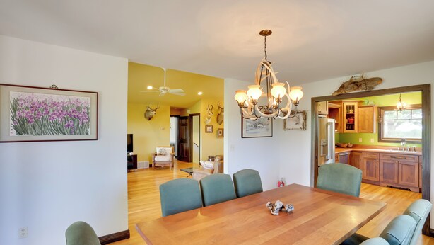 A dining area with a wooden table and green chairs, a chandelier, and a framed floral painting on the wall. - Hermosa Home w/ Black Hills View, Gas Grill & Deck (Hermosa)
