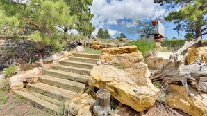 A wooden staircase leading up a rocky hillside with pine trees and a stone structure in the background. - Hermosa Home w/ Black Hills View, Gas Grill & Deck (Hermosa)