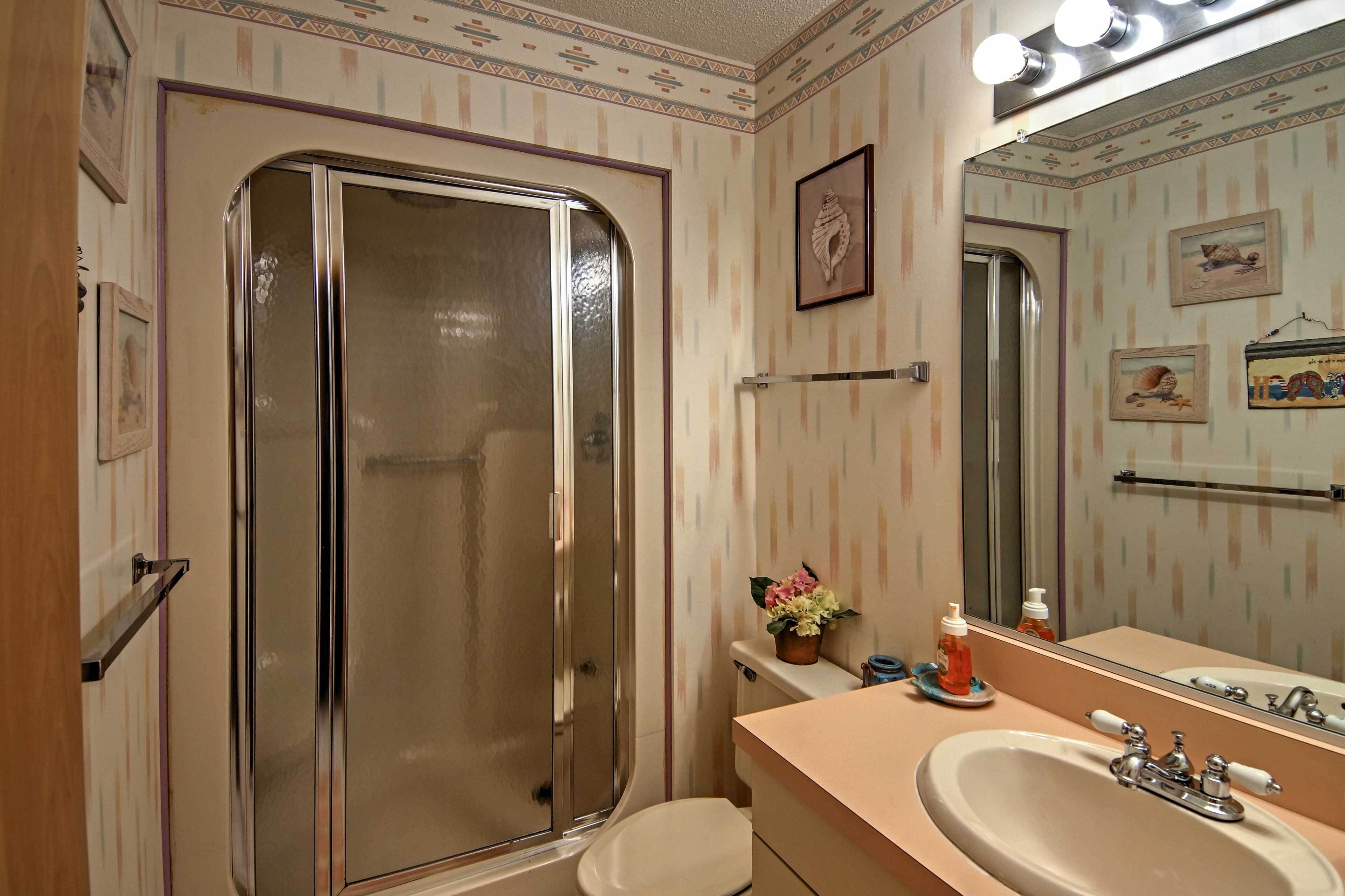 A bathroom with a shower, toilet, sink, and mirror.