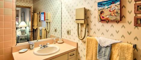 A bathroom with a sink, mirror, towel rack, and a painting of a beach scene.