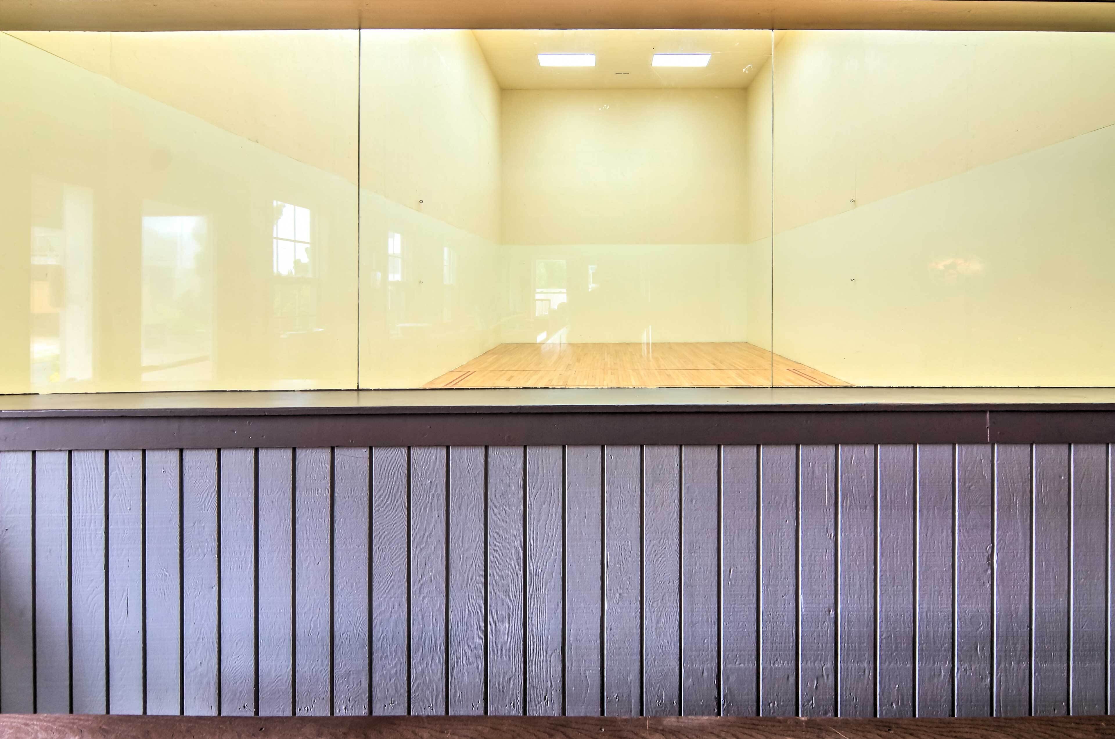 A squash court with a wooden floor and glass walls.