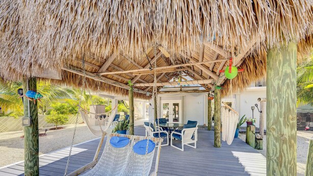 A wooden deck with a thatched roof, a hammock, and a table with chairs. - Canal-front Florida Keys Home w/ Dock! (Tavernier)