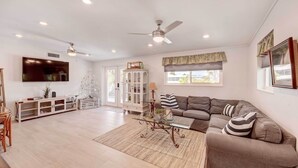 A spacious living room with a large flat-screen TV, a sectional sofa, a glass coffee table, and a ceiling fan. - Canal-front Florida Keys Home w/ Dock! (Tavernier)