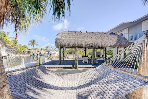 Relax in a serene outdoor space surrounded by lush greenery and a thatched-roof gazebo.