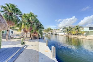 Relax on the waterfront with a hammock set up on the sandy beach, surrounded by palm trees and a modern building in the background.