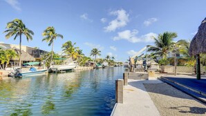 A waterfront area with boats docked along the water, palm trees, and buildings with thatched roofs. - Canal-front Florida Keys Home w/ Dock! (Tavernier)