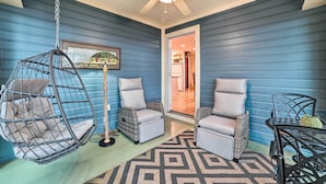 A room with blue walls, a ceiling fan, a hanging chair, two cushioned chairs, a patterned rug, and a table with a pineapple decoration. - Waterfront Cheboygan Home w/ Fire Pit (Cheboygan)