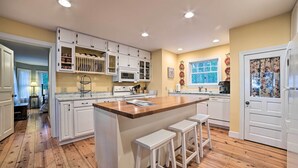 A kitchen with white cabinets, a wooden island with stools, a microwave, and a window with a view. - Waterfront Cheboygan Home w/ Fire Pit (Cheboygan)