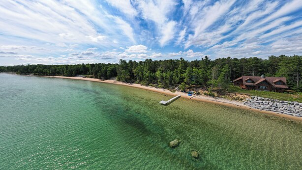 A lakeside property with a dock, clear water, and a cabin surrounded by trees. - Waterfront Cheboygan Home w/ Fire Pit (Cheboygan)