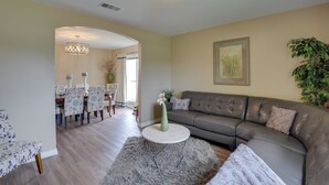 A living room with a grey sofa, a round coffee table, and a dining area with patterned chairs.