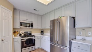 A modern kitchen with white cabinets, stainless steel appliances, and a wooden floor.