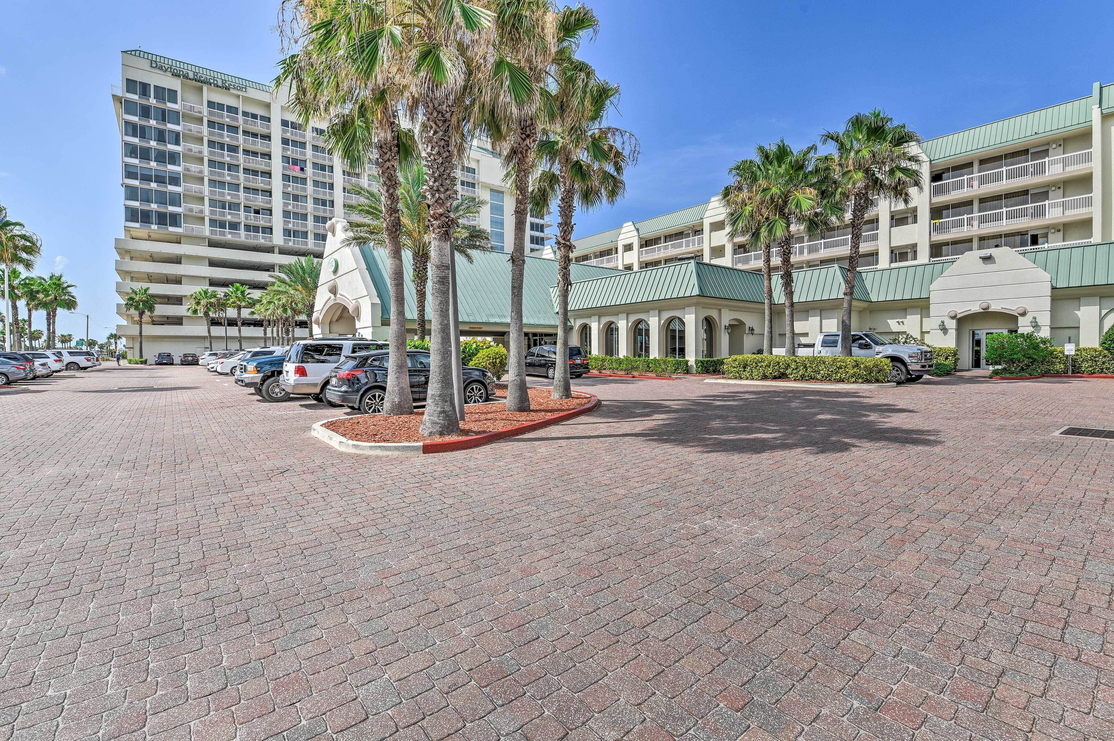 A hotel with a parking lot, palm trees, and a multi-story building with balconies.