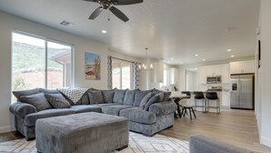 A spacious living room with a large sectional sofa, ottoman, and a dining area with chairs. - Sleek + Modern Home Rental Near Red Cliffs! (Washington)