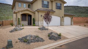 A two-story house with a garage, a landscaped front yard with rocks and a tree, and a hilly backdrop. - Sleek + Modern Home Rental Near Red Cliffs! (Washington)