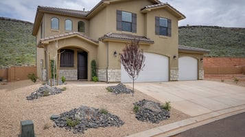 A two-story house with a garage, a landscaped front yard with rocks and a tree, and a hilly backdrop.