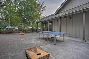 An outdoor area with a ping pong table, a wooden table, and a brick floor.