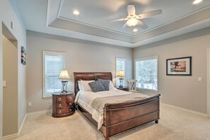 A bedroom with a large bed, two bedside tables, a ceiling fan, and two windows with blinds.