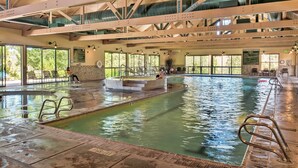 Une piscine intérieure à l’eau claire, dotée de rampes en métal et d’un plafond haut avec des poutres apparentes.