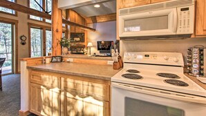 A kitchen with wooden cabinets, a microwave, a stove, and a large window. - Klamath Falls Cabin Retreat w/ Deck & Grill! (Klamath Falls)