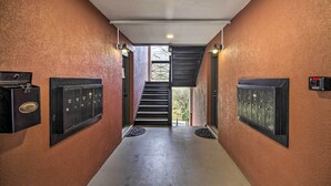 Un couloir avec un escalier menant à un espace extérieur, où se trouvent deux boîtes aux lettres et une porte de chaque côté.