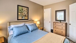 Une chambre à coucher avec un lit, une table de chevet avec une lampe, une commode et un tableau encadré au mur.