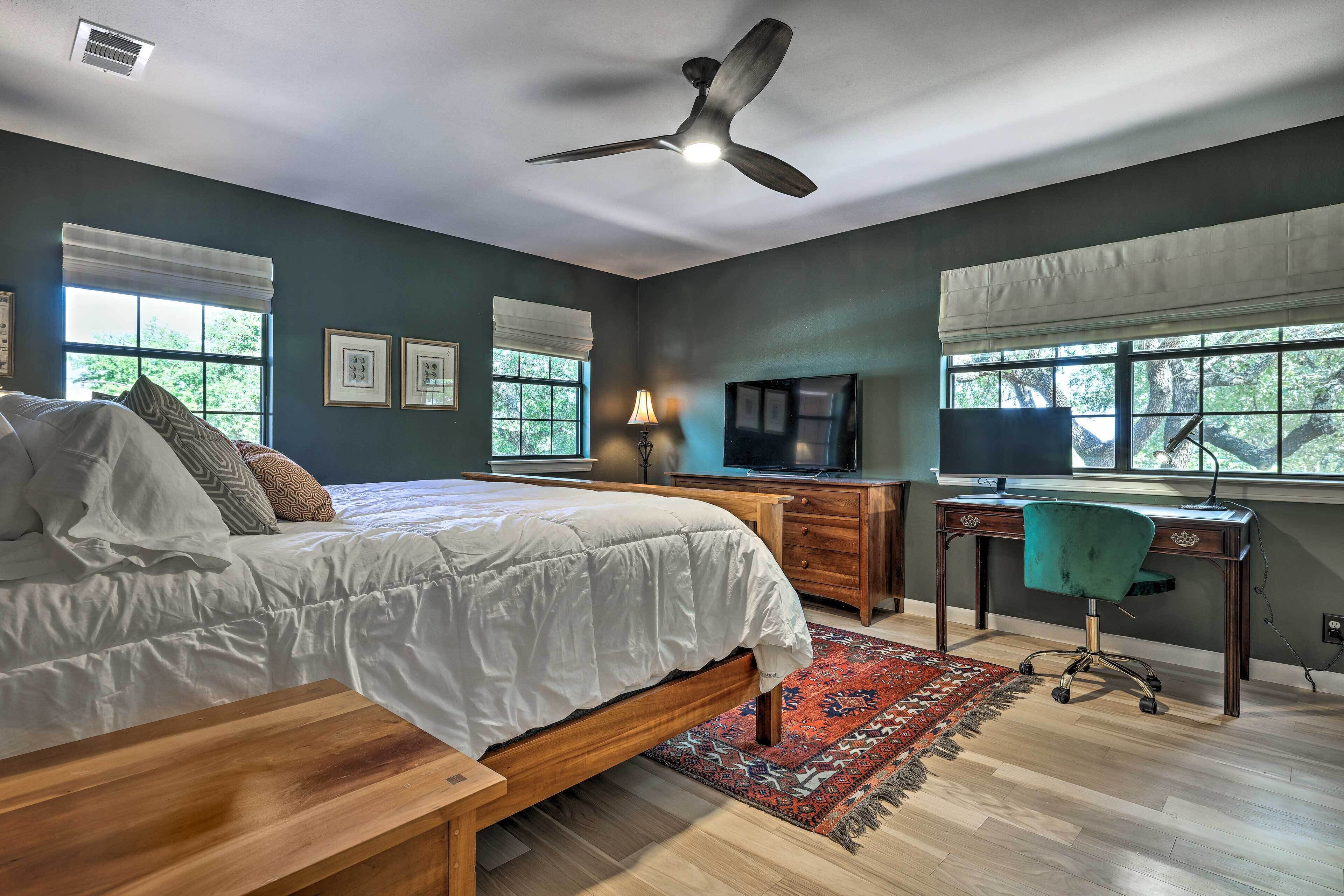 A bedroom with a bed, a desk, a chair, a TV, and a ceiling fan.