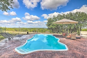 A swimming pool with lounge chairs and an umbrella, surrounded by trees and a clear sky. - Dripping Springs Cabin w/ Pool, Hill Country Views (Dripping Springs)