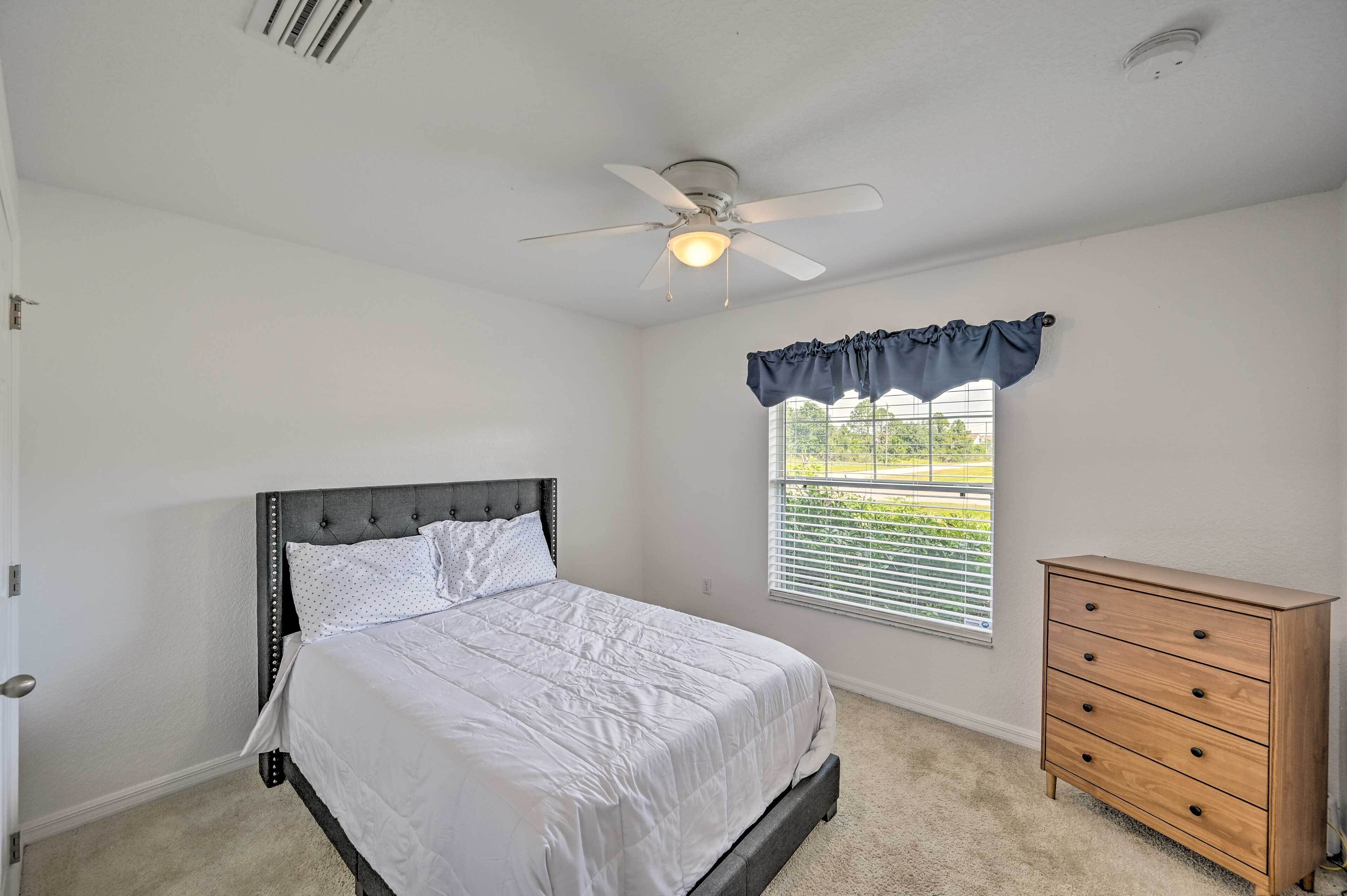 A bedroom with a bed, a dresser, a ceiling fan, and a window with blinds.