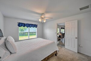 A bedroom with a bed, a ceiling fan, a window with a blue valance, and a door leading to another room.