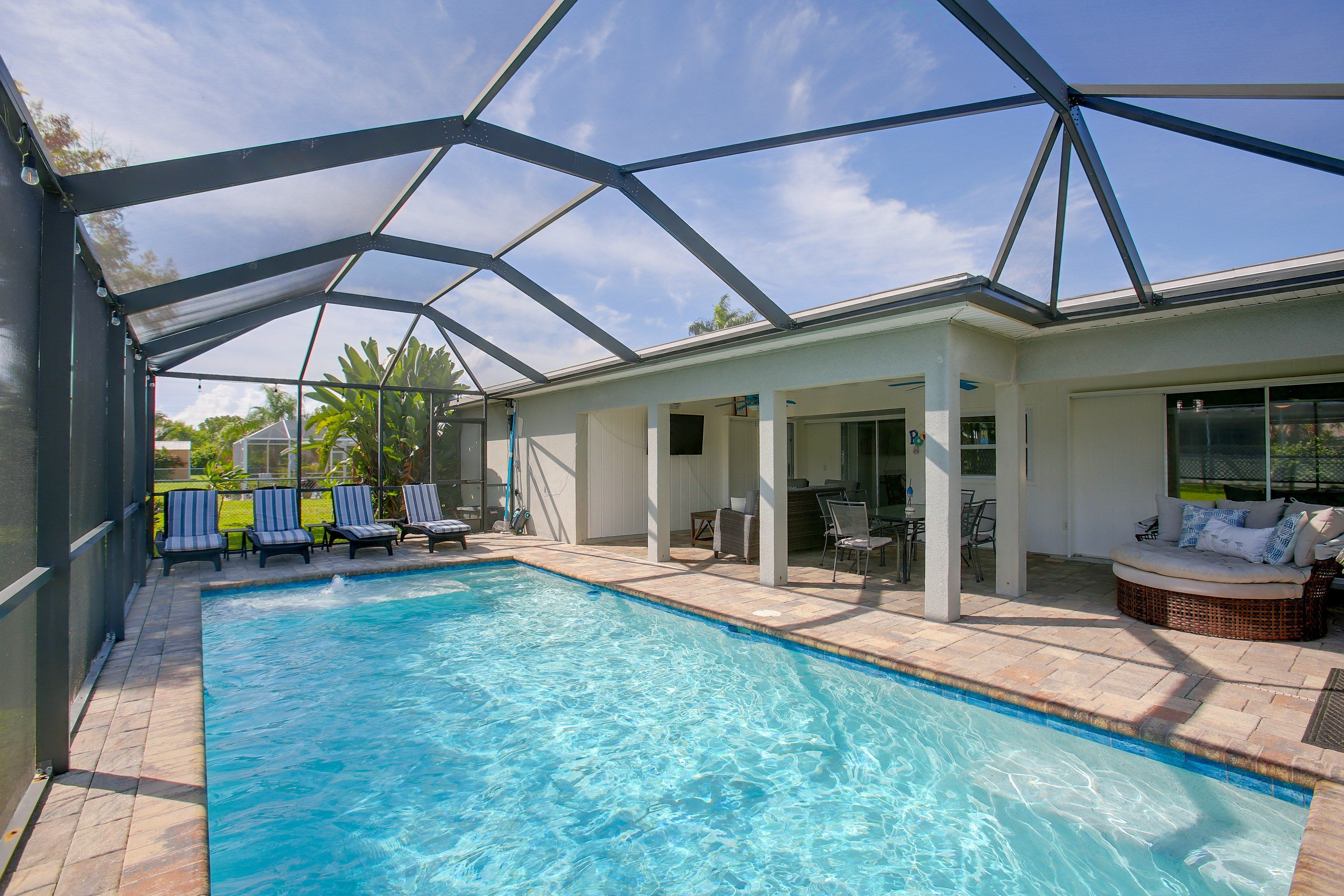 A swimming pool with a covered patio area, lounge chairs, and a seating area with cushions.