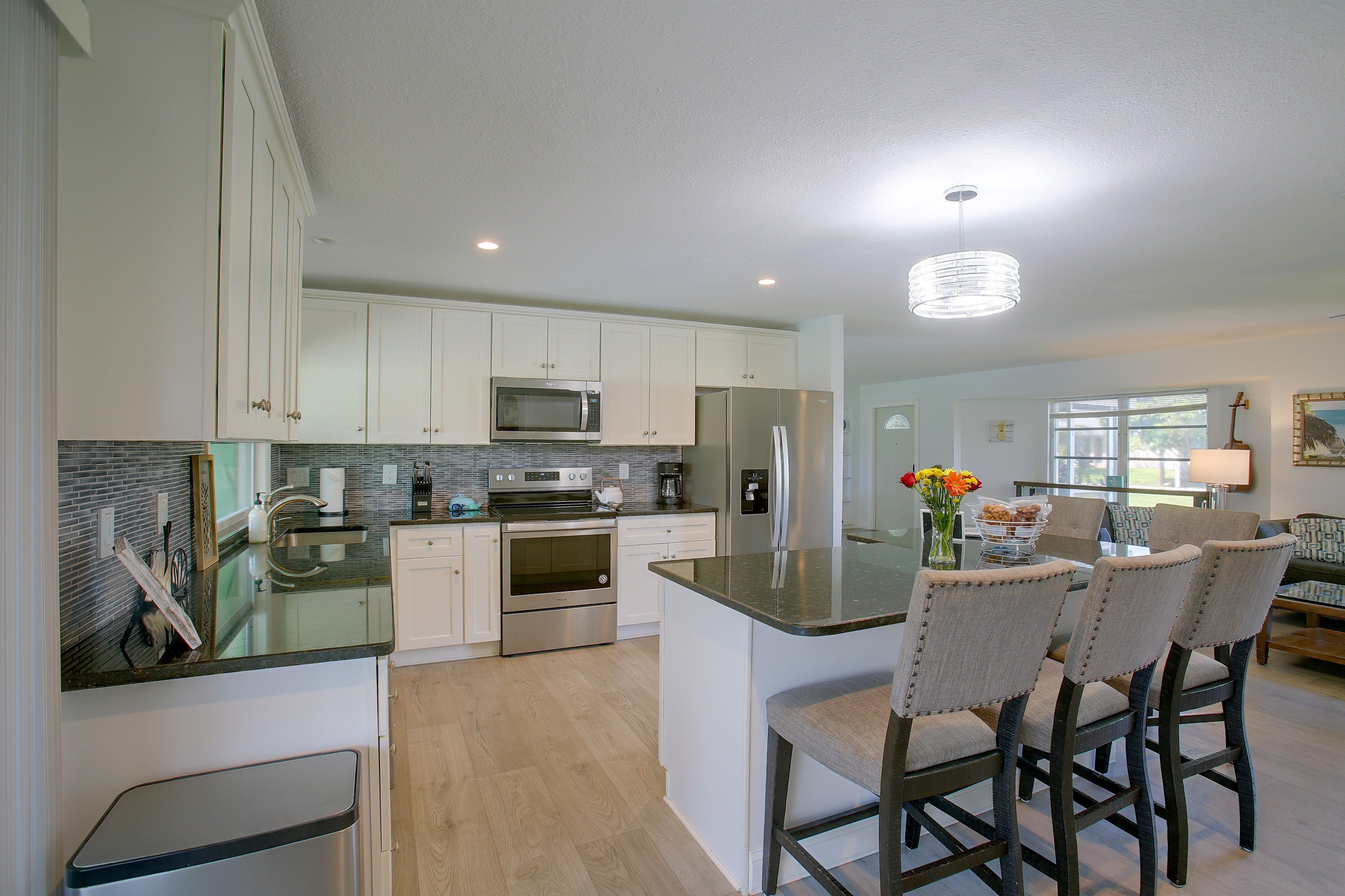 A modern kitchen with stainless steel appliances, a central island with bar stools, and a dining area with a view.