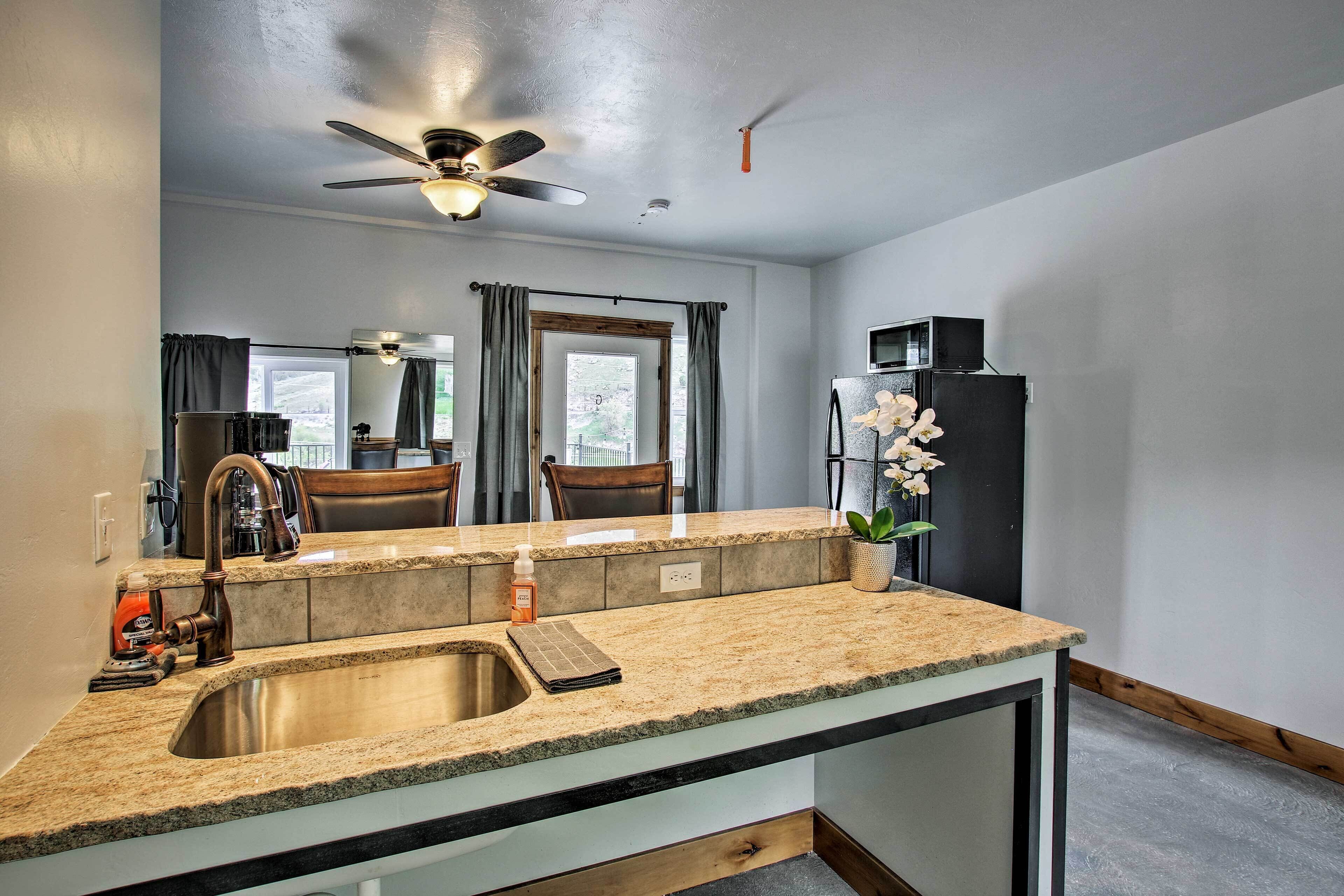 A kitchen with a granite countertop, stainless steel sink, and a ceiling fan.