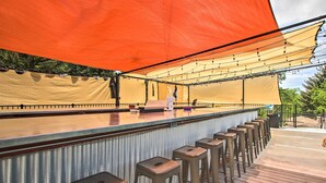 Un espace bar extérieur doté d’un long comptoir, de nombreux tabourets et d’un grand auvent offrant de l’ombre.