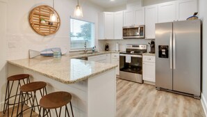 A modern kitchen with white cabinets, a stainless steel refrigerator, a built-in oven, and a granite countertop. There are three wooden stools and a hanging light fixture. - Cozy Rockport Vacation Rental Near Fishing! (Rockport)