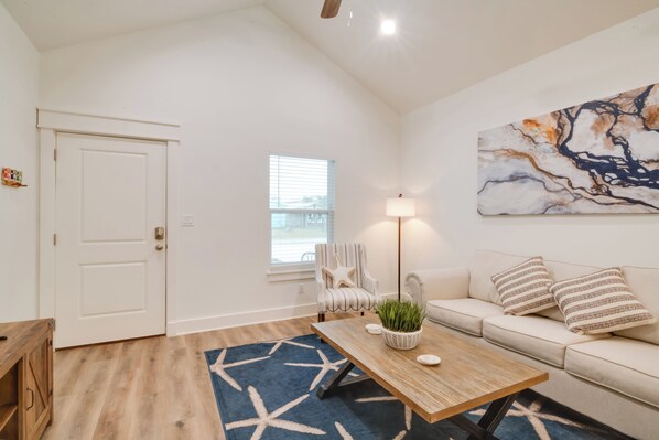 Una sala de estar con una mesa de centro de madera, un sofá color beige, una silla con forma de estrella de mar, un tapete azul y un cuadro en la pared.