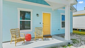A light blue house with a yellow door, two wicker chairs, and a red basket on the porch. - Cozy Rockport Vacation Rental Near Fishing! (Rockport)