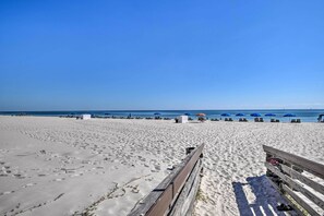 Une plage avec une promenade en bois menant à l’eau, bordée de parasols bleus et de chaises longues.