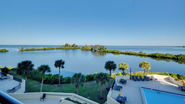 A poolside area with lounge chairs, a small pool, and a view of a calm body of water with an island in the distance. - Gulf-front Views: Coastal Hudson Condo! (Hudson)
