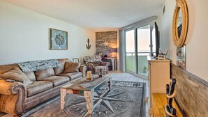 A living room with a brown leather sofa, a coffee table with a compass design, and a large window offering a view of the outdoors. - Gulf-front Views: Coastal Hudson Condo! (Hudson)