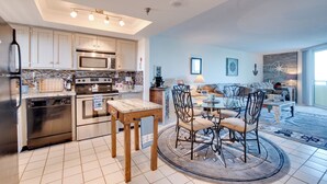A modern kitchen with stainless steel appliances, a dining area with a round table and chairs, and a living room with a sofa and coffee table. - Gulf-front Views: Coastal Hudson Condo! (Hudson)