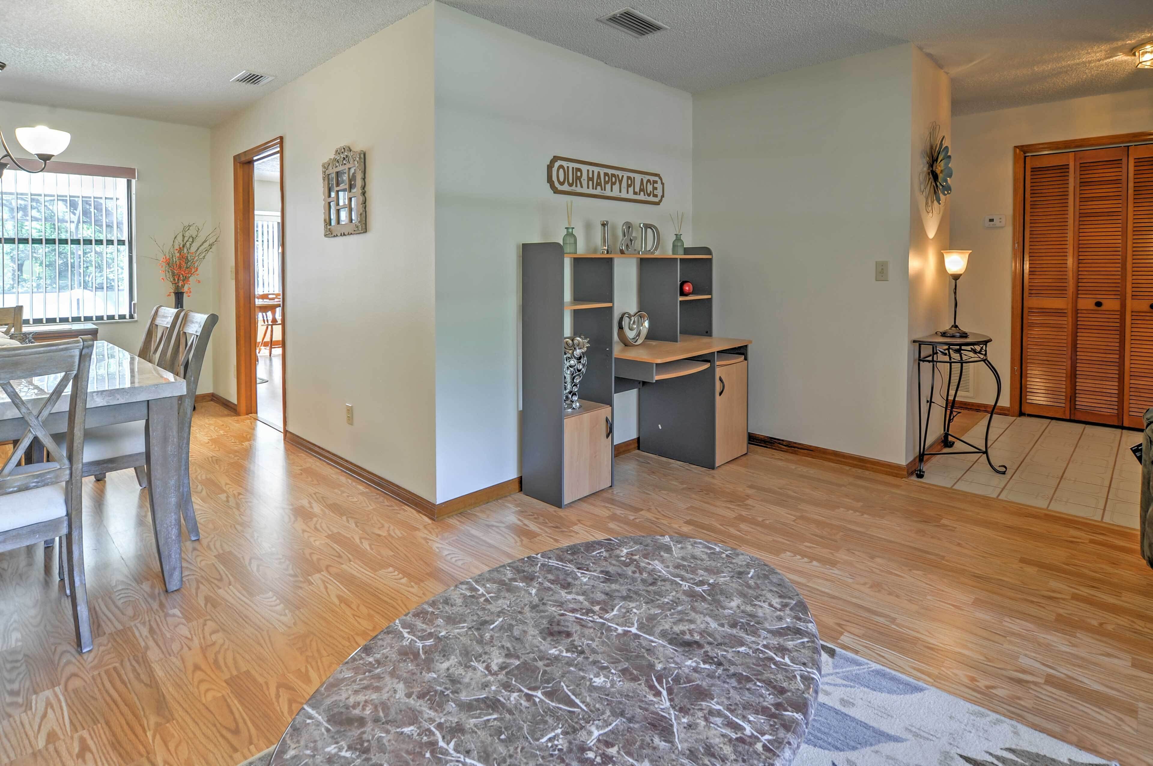 A modern living room with a dining area, a marble rug, wooden flooring, and a sign reading "OUR HAPPY PLACE".