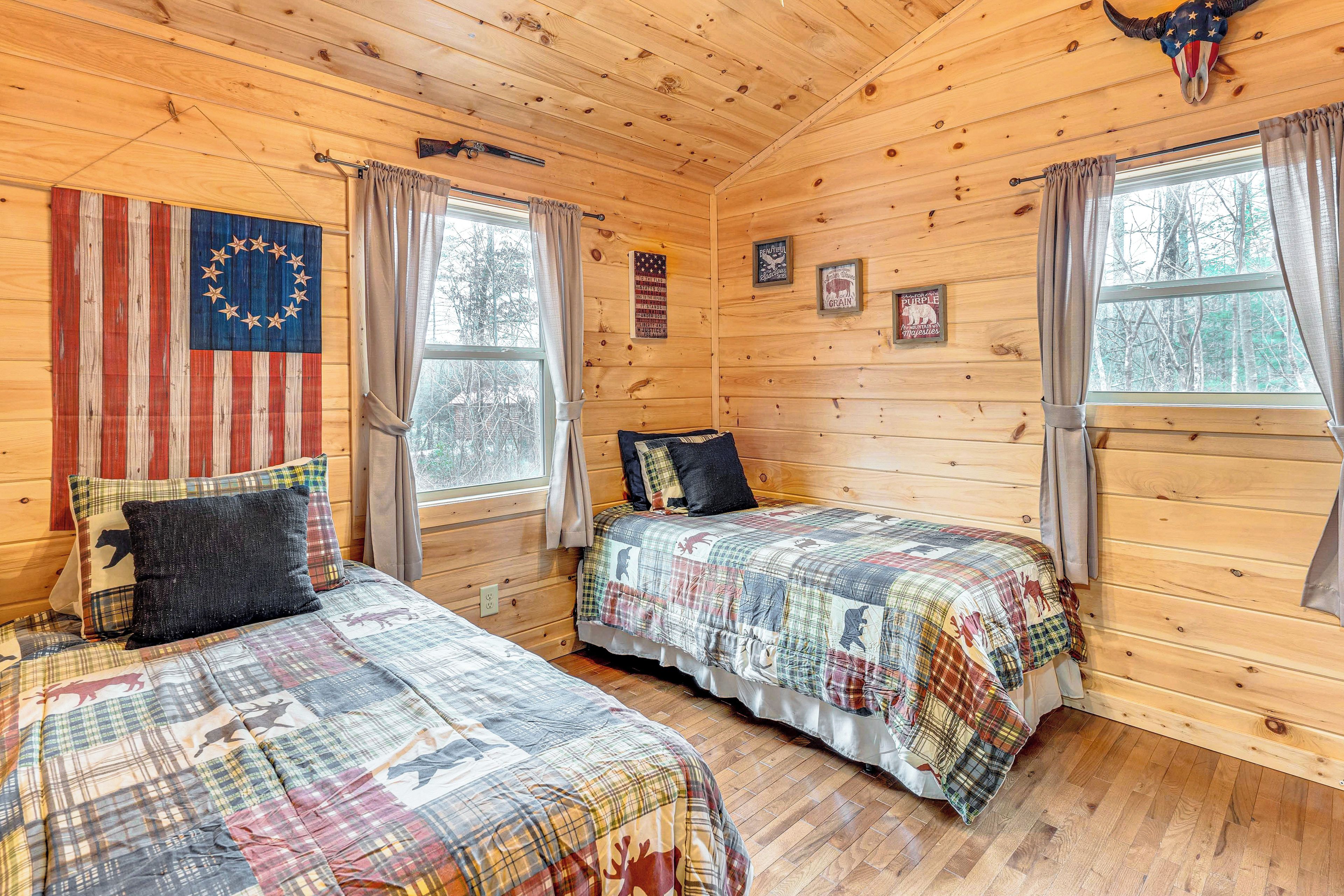 A cabin with two beds, wooden walls, a large window, and a cow skull decoration.