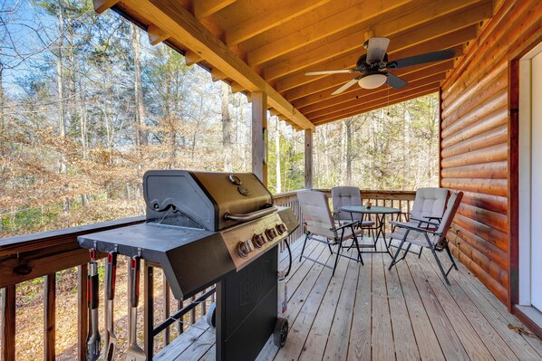 Een overdekt terras buiten met een barbecue, stoelen en een tafel.