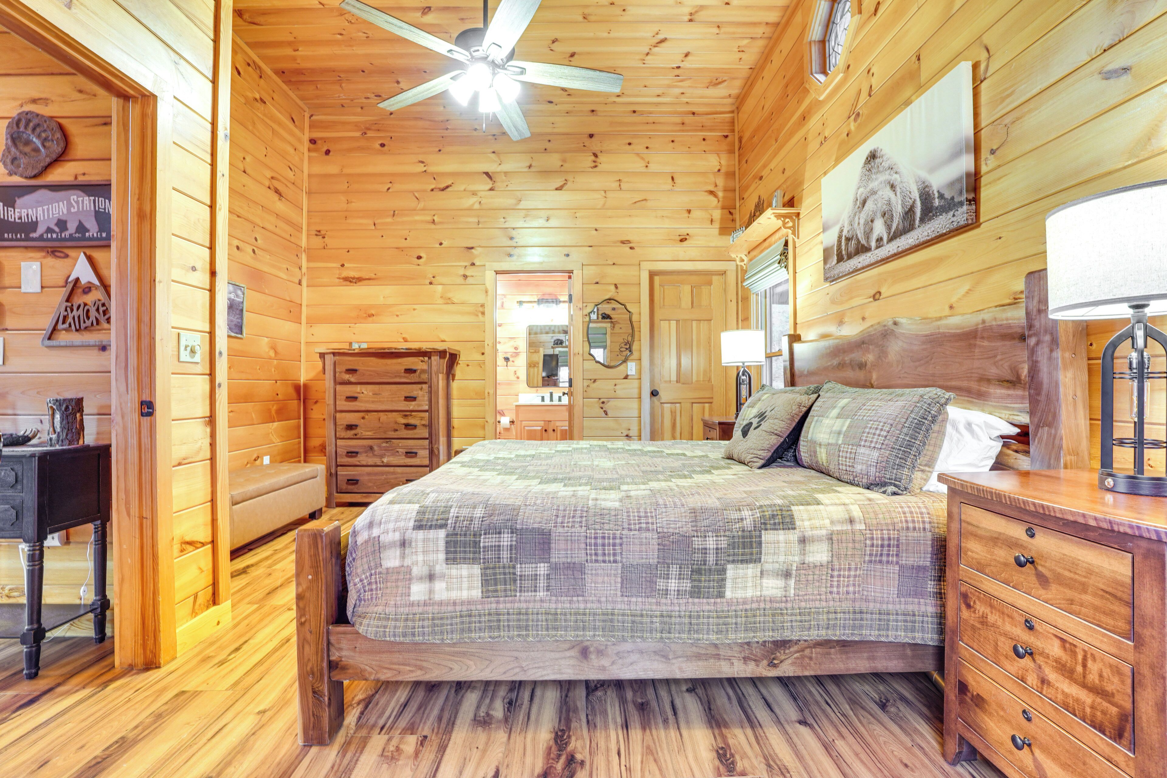 Interior de uma cabana de madeira com cama, cômoda e ventilador de teto.
