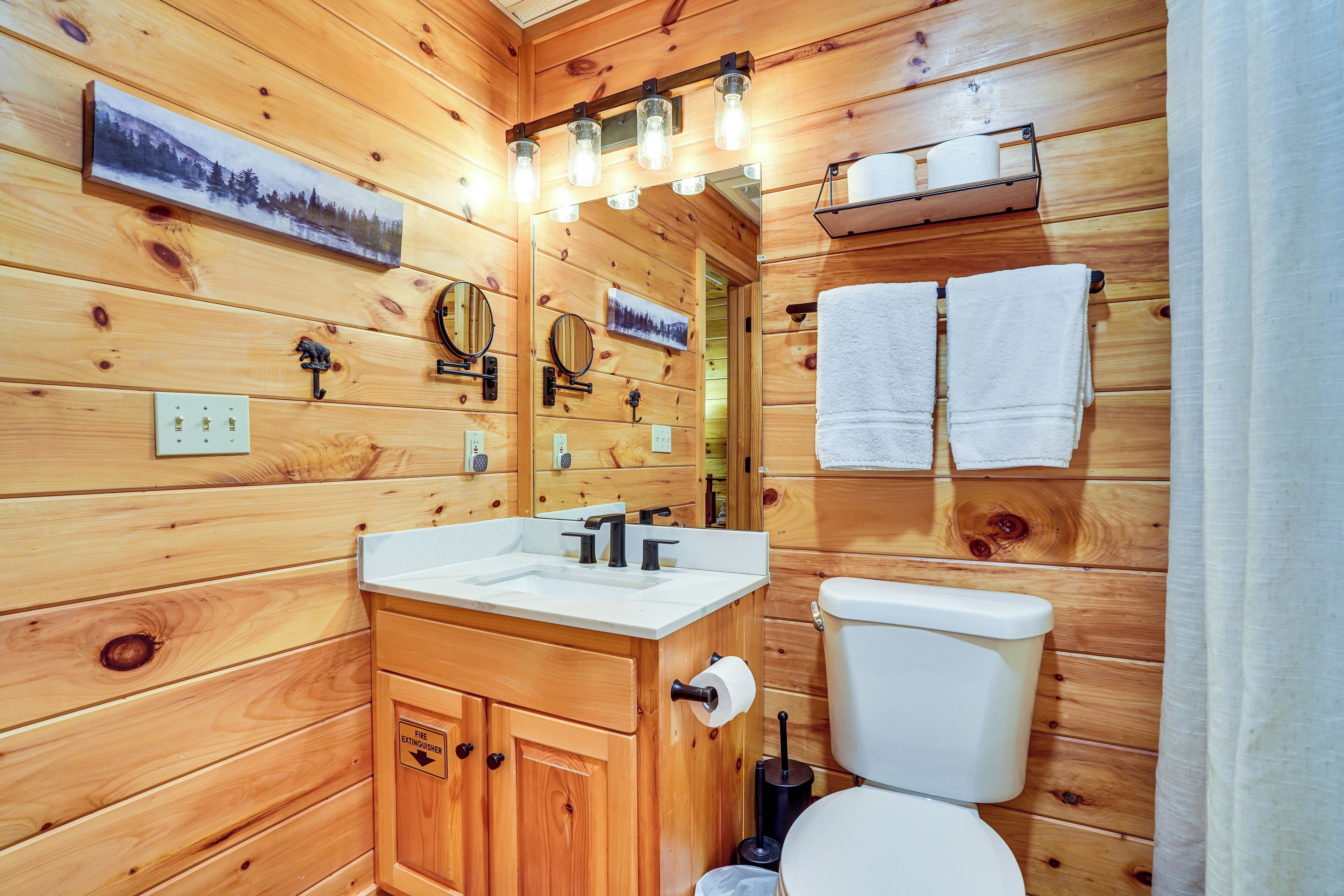 A wooden cabin-style bathroom with a wooden vanity, two sinks, a toilet, and a mirror.