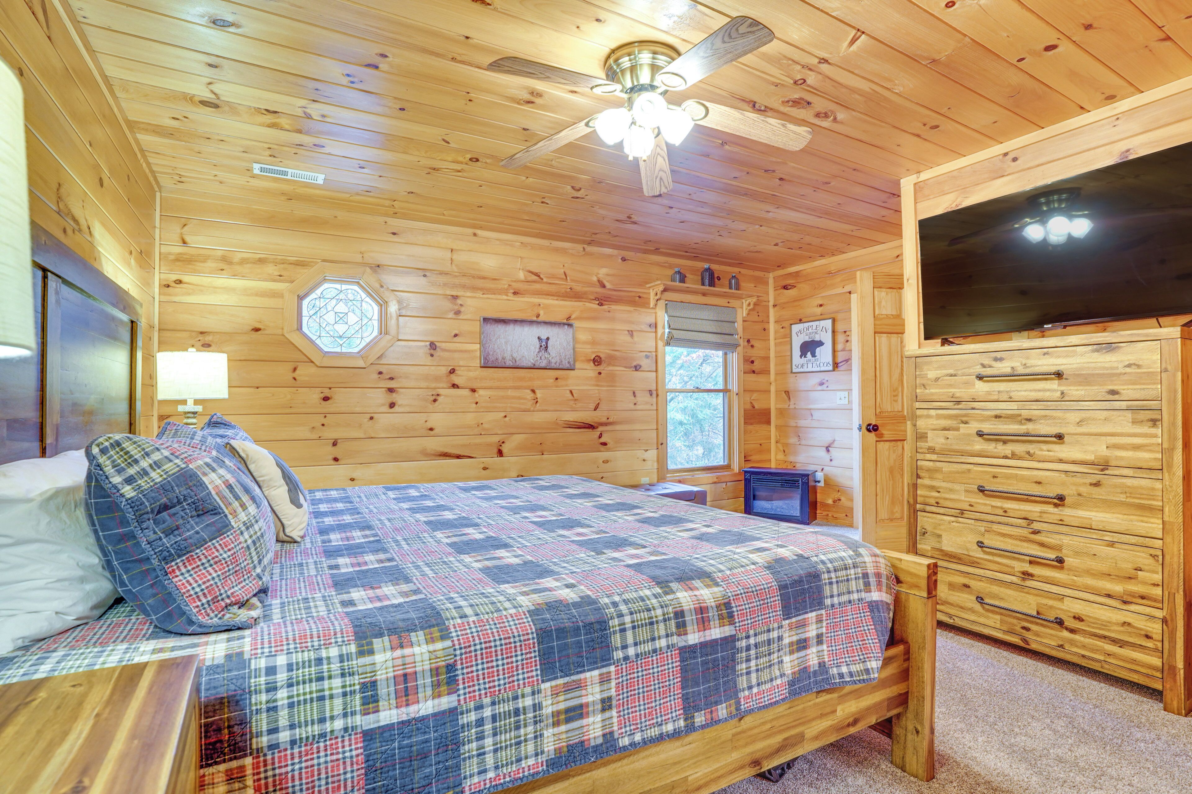 A wooden cabin bedroom with a bed, a ceiling fan, a dresser, and a window.