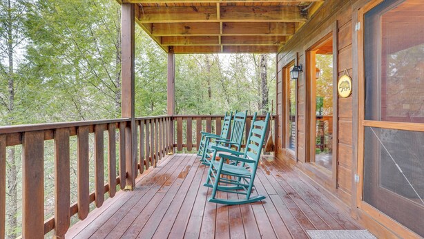 Een houten terras met schommelstoelen, een overdekt gedeelte en uitzicht op het bos.