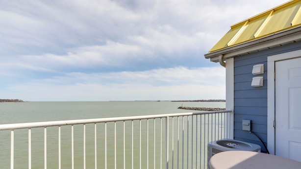 A balcony with a view of a calm body of water, a white railing, a small table, and a chair. - Waterfront Middle Bass Condo w/ Lake Erie Views! (Put-in-Bay)