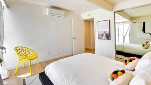 Une chambre à coucher moderne avec un grand lit, une chaise jaune vif et un miroir qui reflète le lit.
